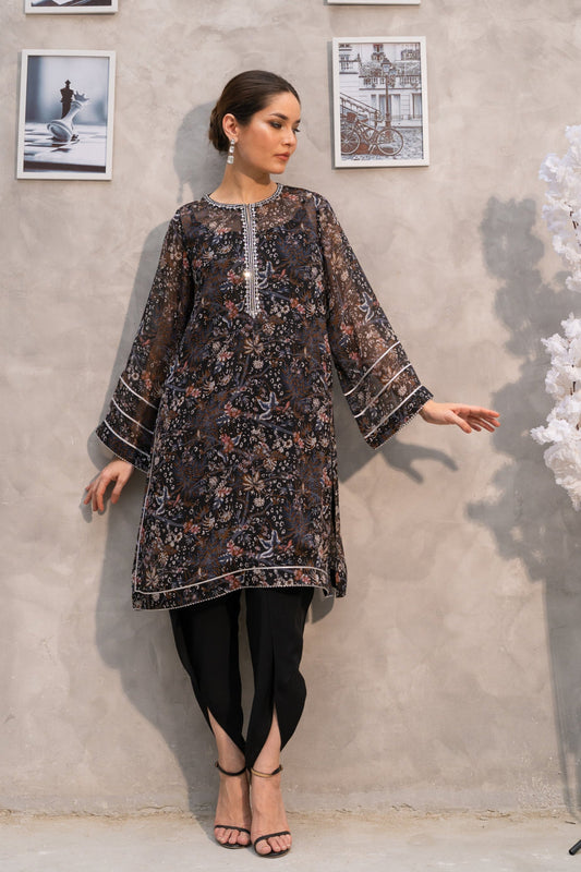 Woman in a patterned dress standing against a gray wall with framed pictures.