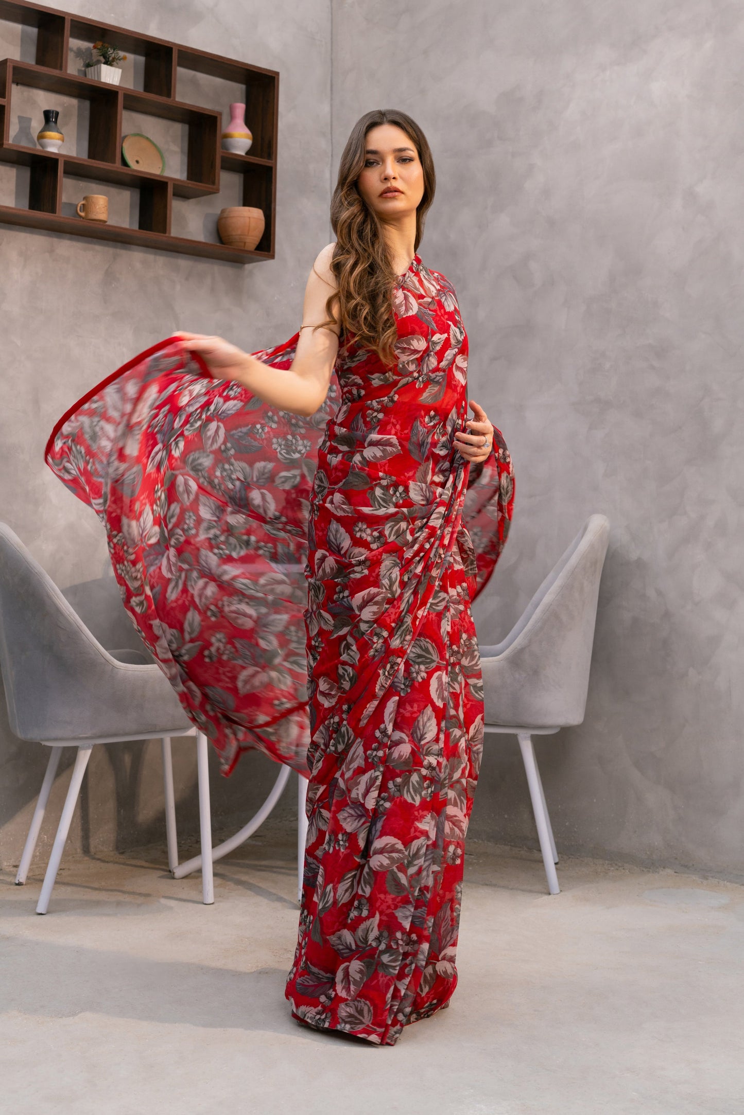 Woman in a red floral dress standing in a modern interior setting with gray walls and a window.