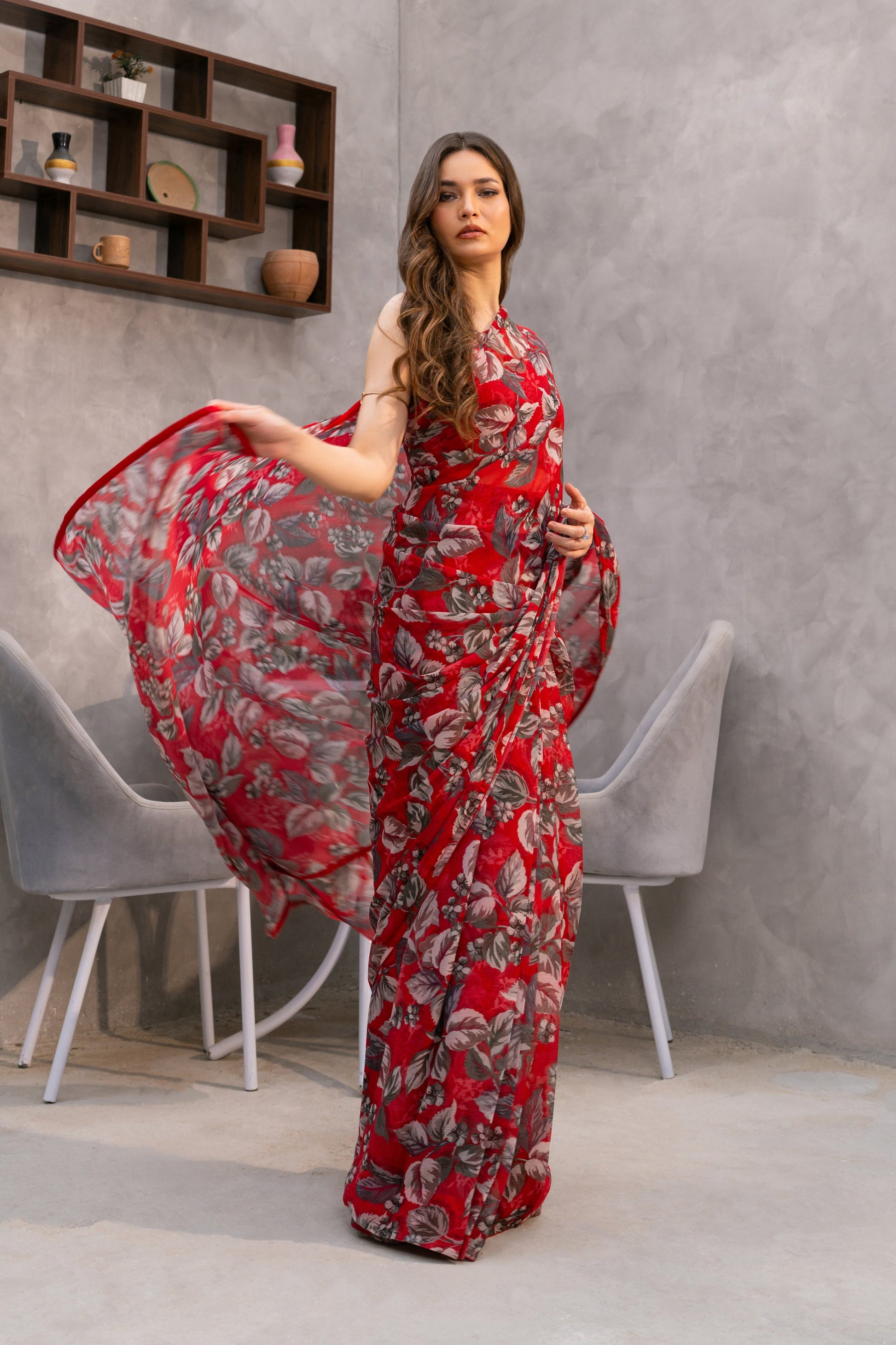Woman in a red floral dress standing in a modern interior setting with gray walls and a window.
