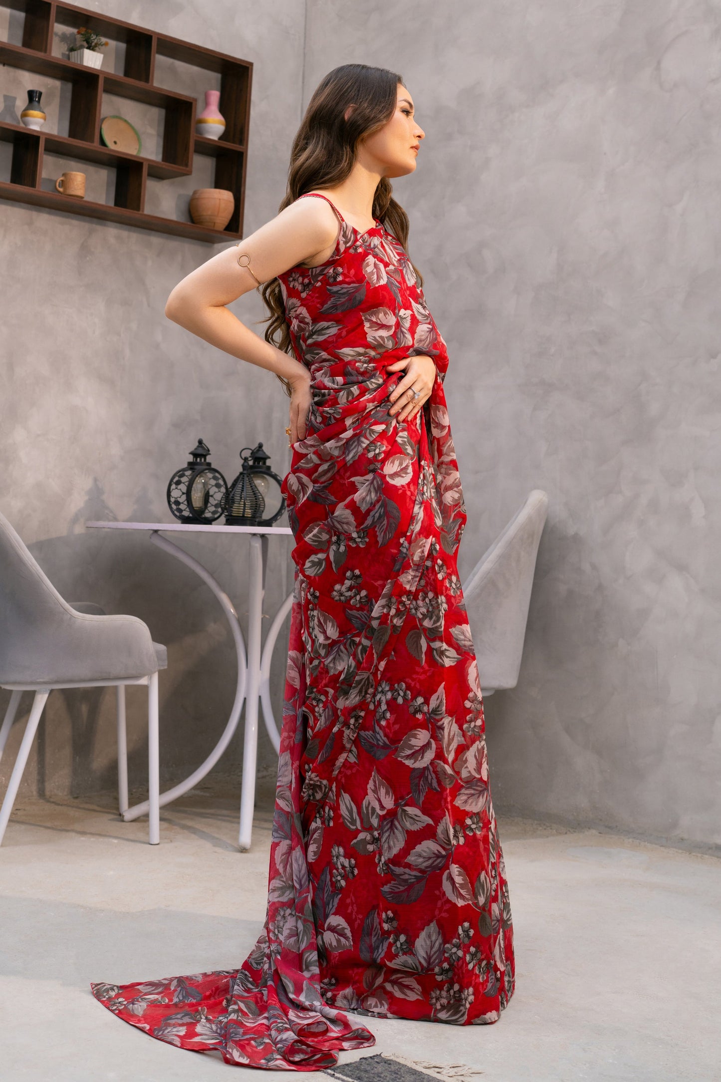 Woman in a red floral dress standing in a modern interior setting with gray walls and a window.