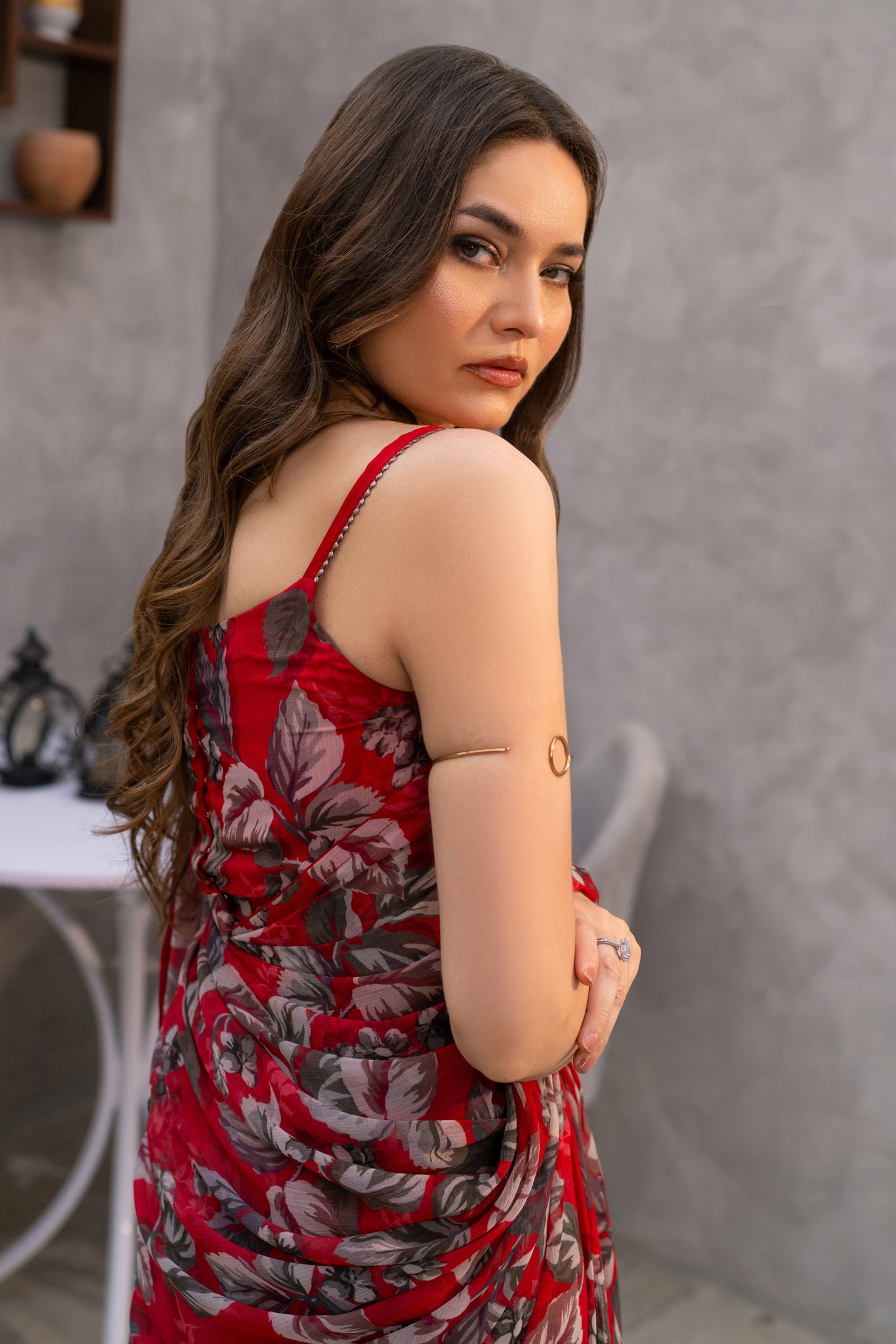 Woman in a red floral dress standing in a room with a gray wall and small table.