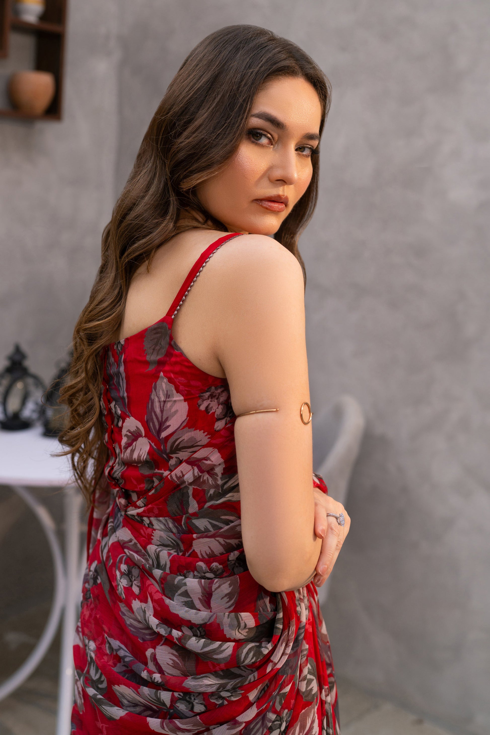 Woman in a red floral dress standing in a room with a gray wall and small table.