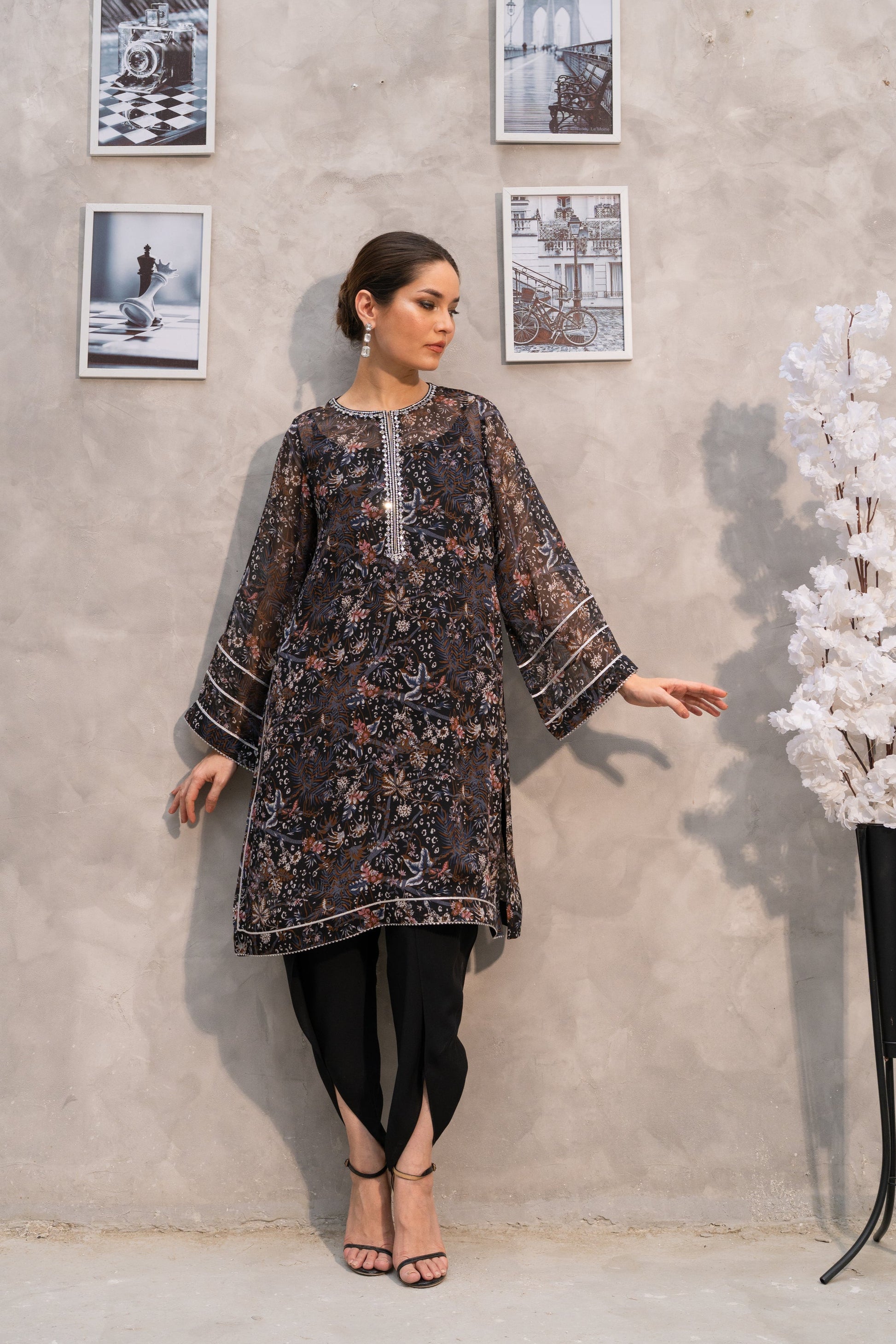 Woman in a patterned dress standing against a gray wall with framed pictures.