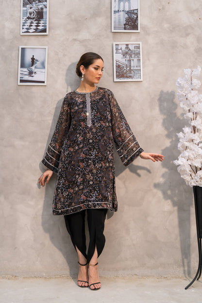 Woman in a patterned dress standing against a gray wall with framed pictures.
