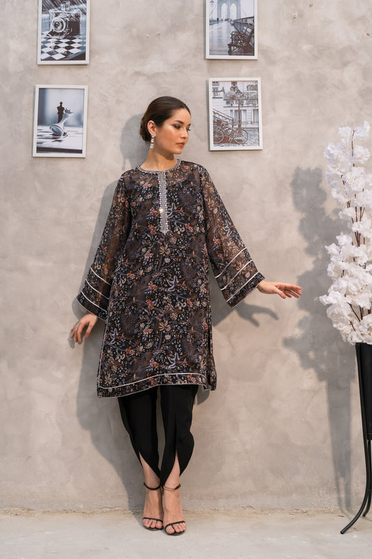 Woman in a patterned dress standing against a gray wall with framed pictures.