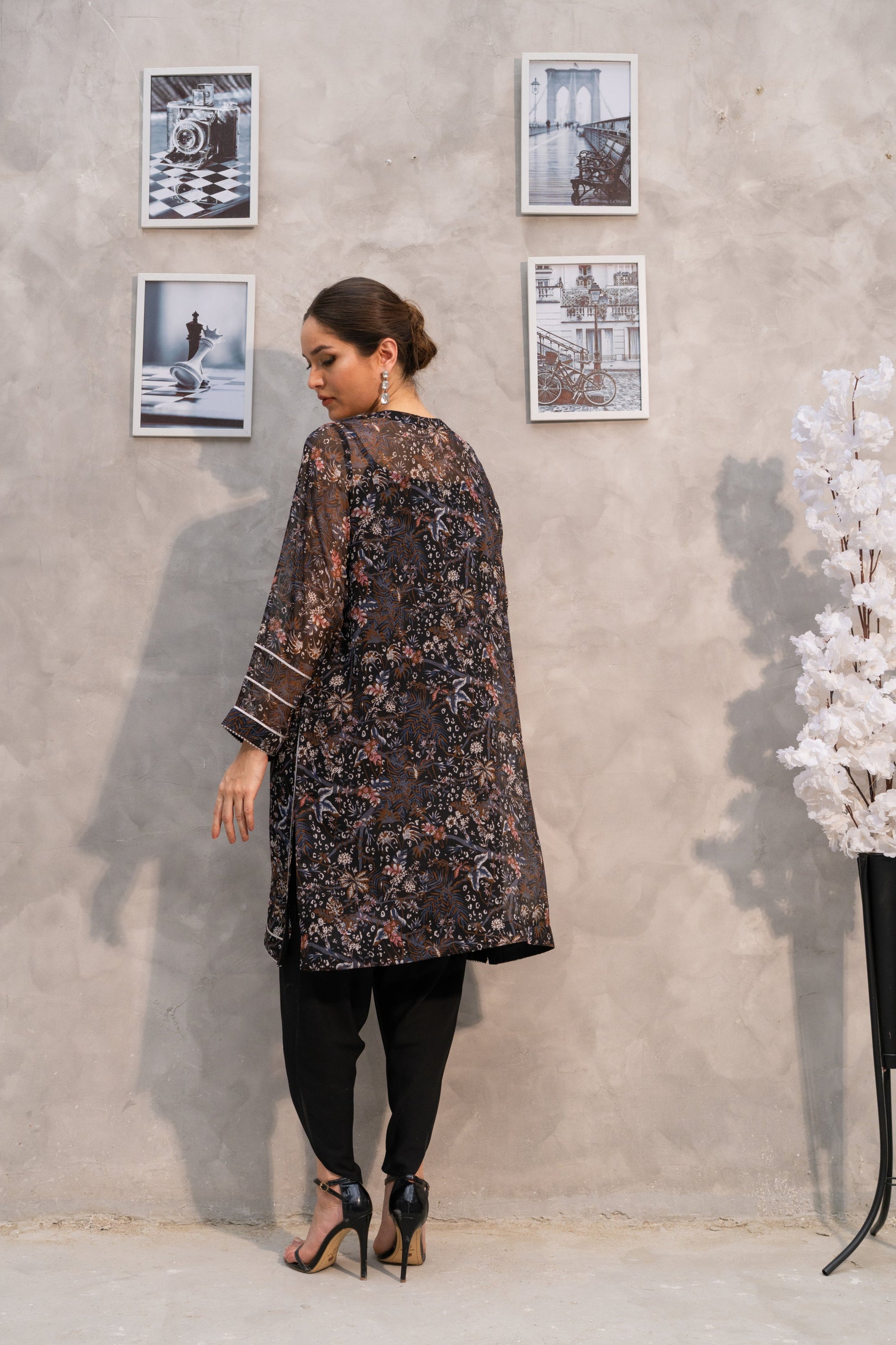 Woman in a floral dress standing against a textured wall with framed pictures.