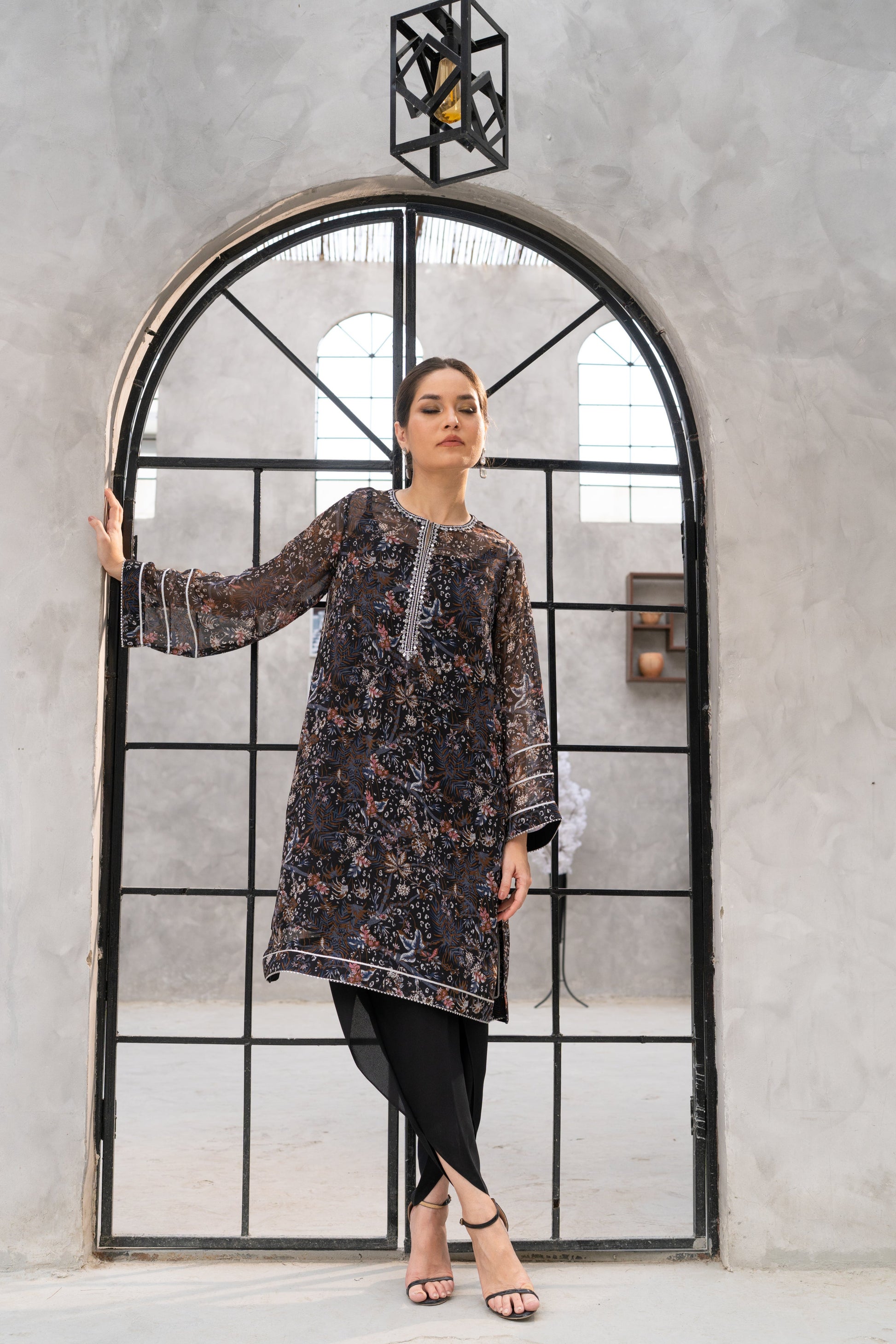 Woman in a patterned dress standing in front of a large mirror with a geometric frame.