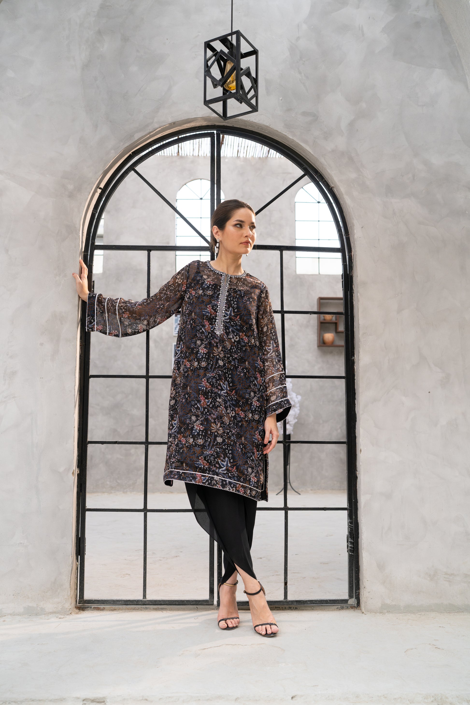 Woman in a patterned dress standing in front of a large mirror with a geometric frame.