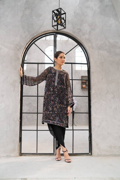 Woman in a patterned dress standing in front of a large mirror with a geometric frame.